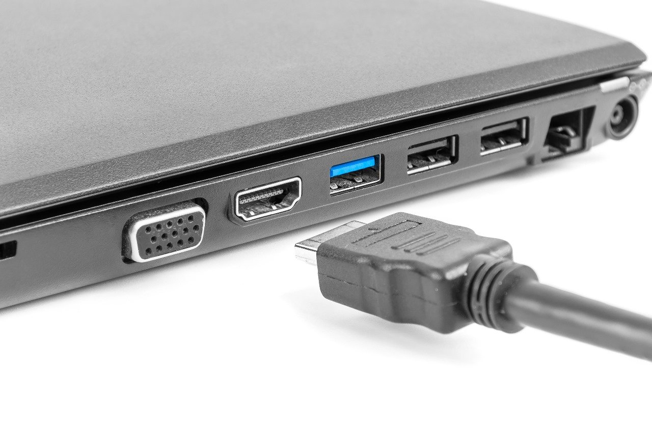 Lateral de notebook mostrando as entradas VGA, HDMI e USB, com cabo HDMI pronto para conectar